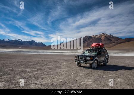 Truck driving through a desert with a lake and a volcano in the background and a blue sky Stock Photo