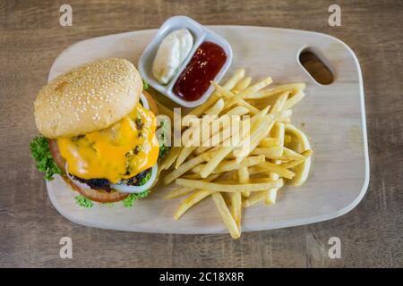 Home made burger with beef, onion, tomato, lettuce and cheese. Fresh burger closeup with potato fries and condiments. Stock Photo