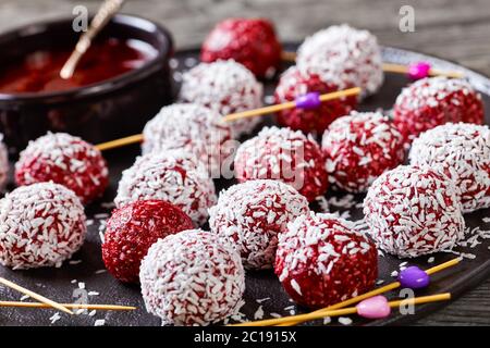 Energy berry bliss balls of desiccated coconut mixed with peanut butter and fresh mix of summer raspberries, blackberries, blueberries on a black plat Stock Photo