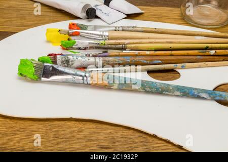 Art palette with colourful art brushes with orange, yellow and green paint on wooden background Stock Photo