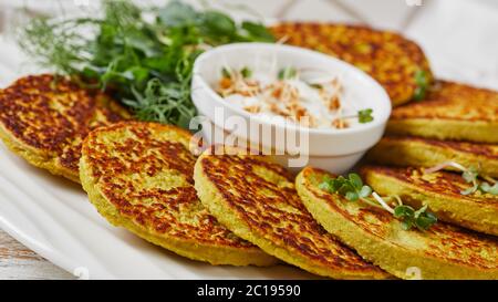 green pea and oatmeal pancakes on a white platter with plain greek yogurt sauce with fresh sprouts of pea and wheat, healthy diet concept, horizontal Stock Photo