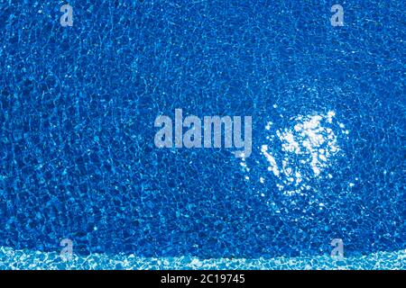 Swimming pool, blue clear water in the outdoor pool, with sun flare on the surface. Background of blue water in the pool. Ripples on the surface of th Stock Photo