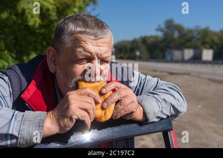 Portrait of hungry senior driver eating patty leaning his elbows on his car door Stock Photo