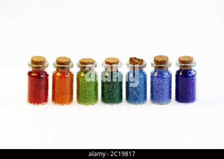 Seven tiny glass bottles with a cork stopper, filled with a rainbow colours of beads, on a white background Stock Photo