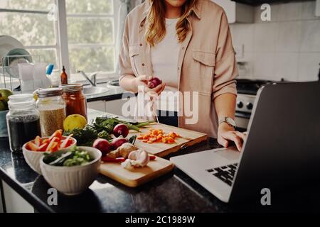 Young female blogger searching online browsing for recipes to prepare salad of fresh vegetables and post on social media in vlog - new hobby during Stock Photo