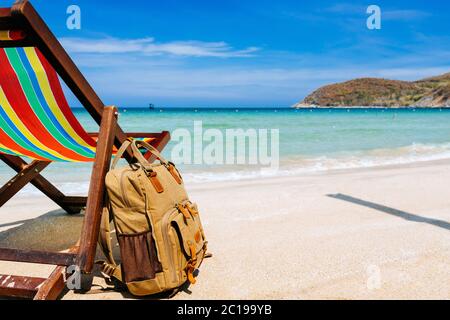 A place for the traveler, freelancer. A deck chair on the sandy shore of a tropical beach overlooking the open sea. a stylish brown backpack standing Stock Photo