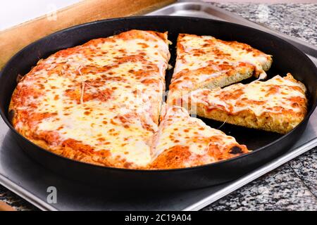 Large freshly prepared Italian margherita pizza sliced in a baking tray on a kitchen counter in closeup high angle Stock Photo