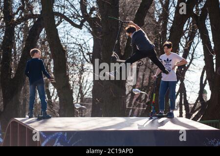 Lviv, Ukraine - March 12, 2020: Kids ride on scooter at skate park. Young boy going airborne with his scooter. Stock Photo