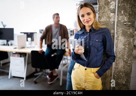 Business woman with a tablet, her co-workers discussing business matters in the background Stock Photo