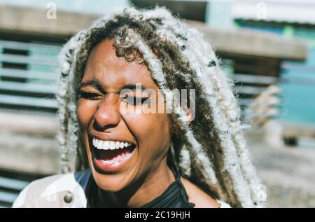 Happy afro girl with blond dreadlocks laughing outdoor with urban city context as background - Millennial black woman having fun outdoor - Soft focus