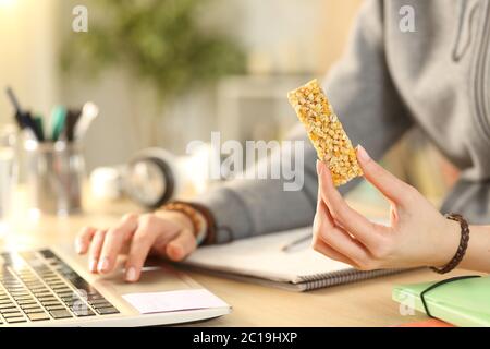 Close up of student girl hands holding snack bar using laptop at home