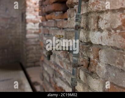 Room in a ruin with dilapidated old brick wall and copper water tap Stock Photo