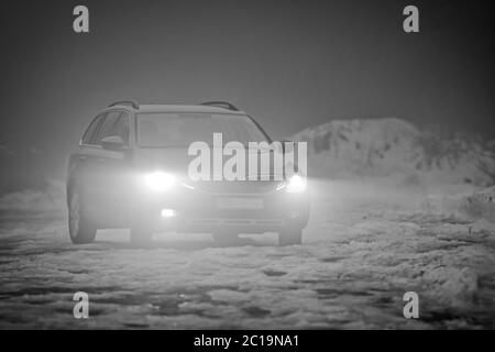 The greyscale photo of car with the lights on in the fog Stock Photo