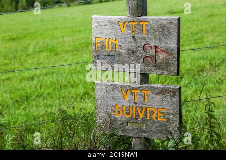 Wooden panel indicating the path for mountain cyclists, in front of a green field. Stock Photo