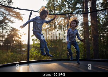 Sweet preteen boy jumping on trampoline making somersaults in the air. Child levitating. Happy child jumping on sunset Stock Photo