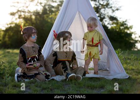 Cute portrait of native american boys with costumes, playing outdoor in the park with hatchet on sunset, summertime Stock Photo