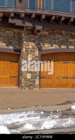 Vertical crop facade of home featuring two hinged wooden garage doors and stone brick wall Stock Photo