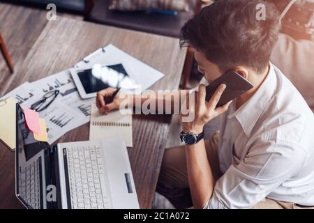 Businessman use mobile phone for talking and right hand use pen for checking data on paper chart, graph. Stock Photo
