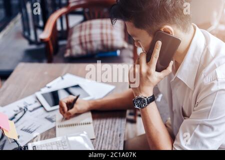 Businessman use mobile phone for talking and right hand use pen for checking data on paper chart, graph. Stock Photo