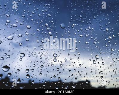 Rain drops on the window glass as background with copyspace for your text, with silhouette of some buildings and thunderstorms sky behind the window Stock Photo