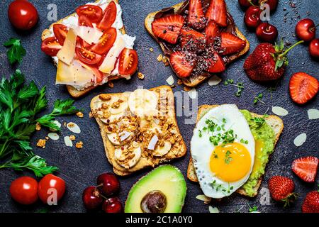 Breakfast different toasts with berries, cheese, egg and fruit, dark background. Stock Photo