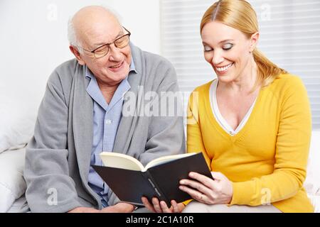 Smiling woman reads stories from a book to a senior
