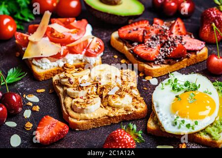 Breakfast different toasts with berries, cheese, egg and fruit, dark background. Stock Photo