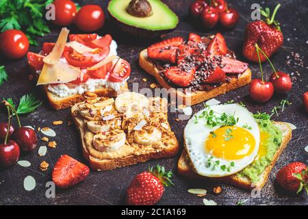 Breakfast different toasts with berries, cheese, egg and fruit, dark background. Stock Photo