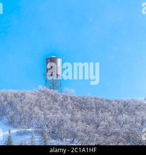 Square Snow covered Wasarch Mountains in winter with water tank tower against blue sky Stock Photo
