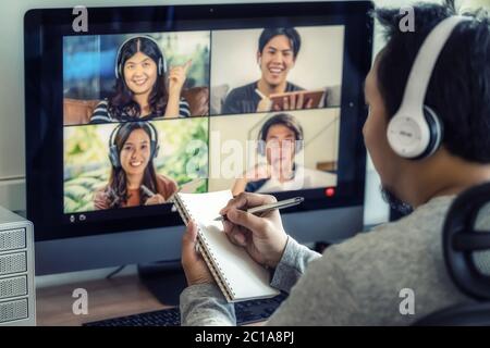 Closeup Asian man hand writing notebook when online learning via video conference with colleague and team building meeting when Covid-19 pandemic,Coro Stock Photo
