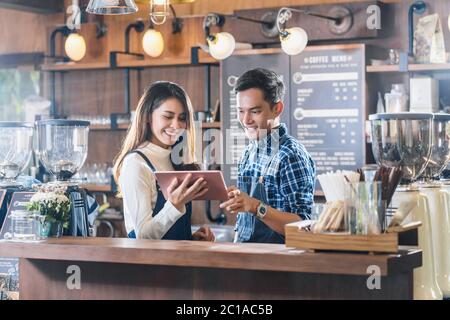 Asian Young Small business owner talking with colleagues and using technology tablet in front of counter bar, entrepreneur and startup, preparing for Stock Photo