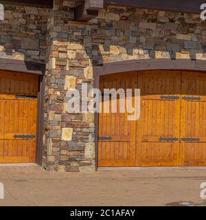 Square frame facade of home featuring two hinged wooden garage doors and stone brick wall Stock Photo