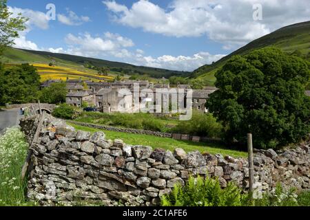 View over traditional dry stone wall to village of Thwaite in Swaledale valley, Thwaite, Yorkshire Dales National Park, North Yorkshire, England, UK