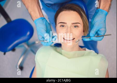 Dentist examining a patient's teeth using dental equipment in dentistry office. Stomatology and health concept. Young handsome male doctor in Stock Photo