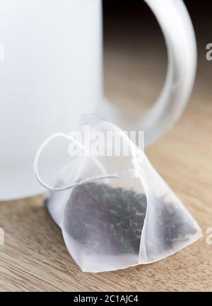 Single bag of elite tea in silk fabric packing and tea mug on a wooden background. Small depth of sh Stock Photo