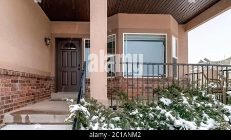 Panorama Snowy evergreens beside stairs that leads to porch of home with front bay window Stock Photo