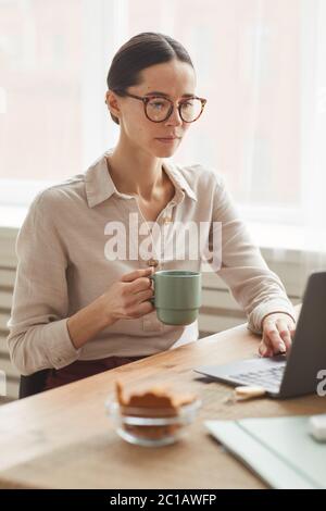 Vertical portrait of elegant businesswoman wearing glasses while using laptop at cozy home office workplace Stock Photo