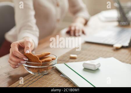 Warm-toned close up of unrecognizable woman taking homemade cookie while working at home, copy space Stock Photo