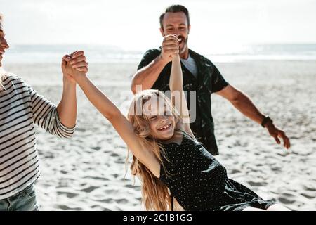 Girl enjoying vacation on beach with her parents. Mother and father holding hands of their girl playing on the beach.