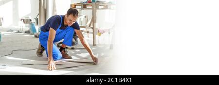 Master is wearing work clothes, is checking horizon of installing tiles, using building level, adjusting, professional repairing work Stock Photo
