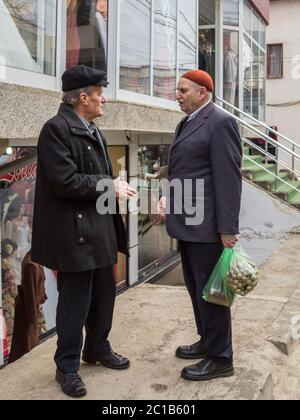 GNJILANE, GJILAN - JANUARY 2, 2016: Old aged retired men, one wearing a traditional hat, discussing in the Gjilan market, in Eastern Kosovo.  Picture Stock Photo
