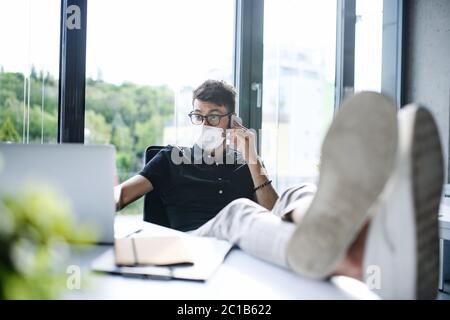 Young man with face masks back at work or school in office after lockdown, having fun. Stock Photo