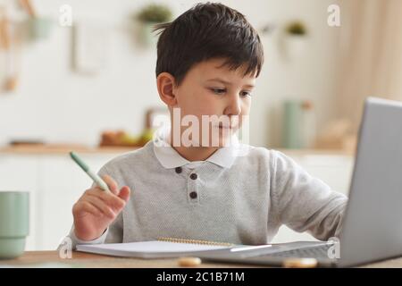 Warm-toned portrait of cute boy studying at home while using laptop sitting at desk in cozy home interior, copy space Stock Photo