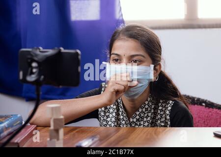 Young Girl in medical face mask talking or having chat with doctor in video conference on mobile phone - telehealth, telemedicine or tele counseling Stock Photo