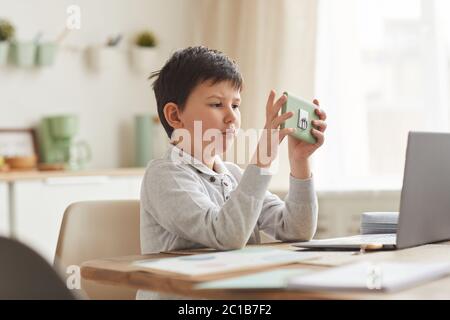 Warm-toned portrait of cute boy using smartphone while studying at home sitting at desk in cozy interior, copy space Stock Photo