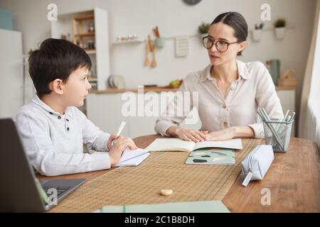 Warm-toned side view portrait of cute boy listening to mom while studying at home in cozy kitchen interior Stock Photo