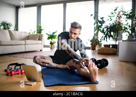 Front view portrait of man with tablet doing workout exercise indoors at home. Stock Photo