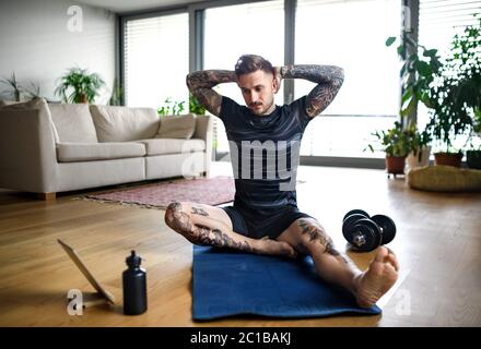 Front view portrait of man with tablet doing workout exercise indoors at home. Stock Photo