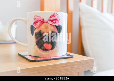 Cup of coffee in cute dog mug on bedside table in a light and airy bedroom Stock Photo