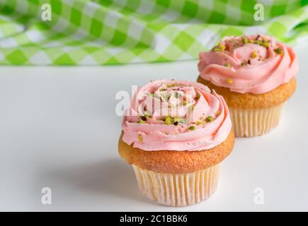 Two pink rose swirled frosted cup cakes with pistachio nut sprinkles on white background with space Stock Photo